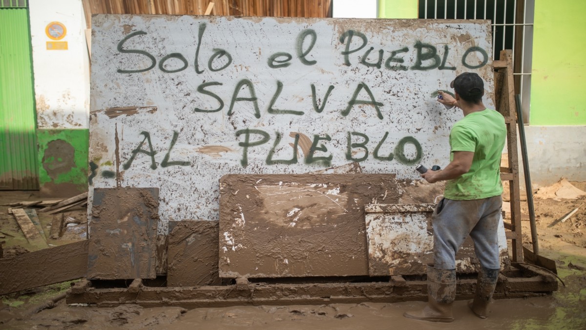 Un voluntario realiza un graffiti en un mural del barrio de El Raval en el que se lee: 'Solo el pueblo salva al pueblo', en Algemesí, València.