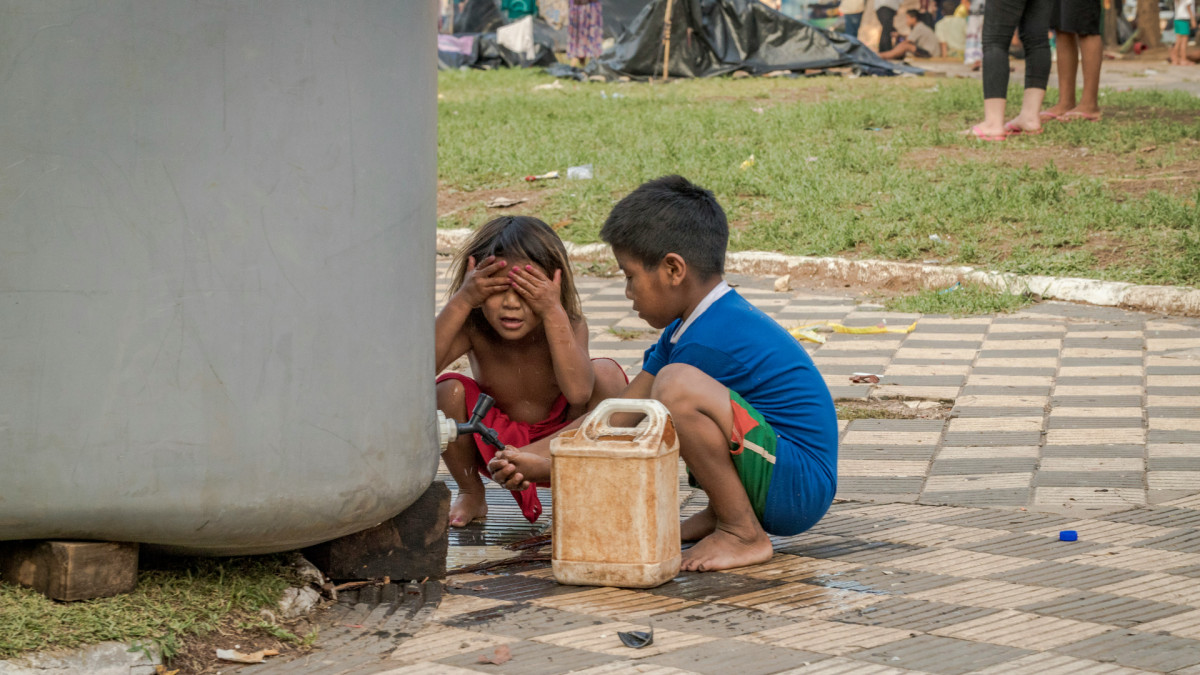 Dos niños consiguen agua de un depósito en una calle de Paraguay.