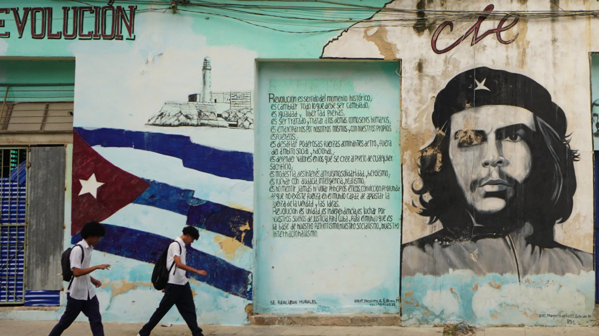 Jóvenes pasean por las calles de La Habana con la bandera nacional y un retrato de el Che Guevara pintados en las paredes.