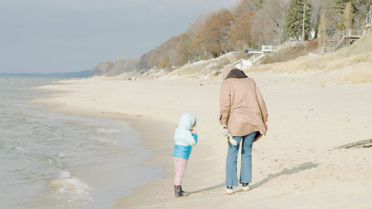 Una niña y su madre pasean por la playa.