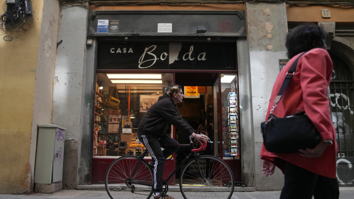 Una persona pasea en bicicleta frente a un comercio local en una calle de Barcelona.