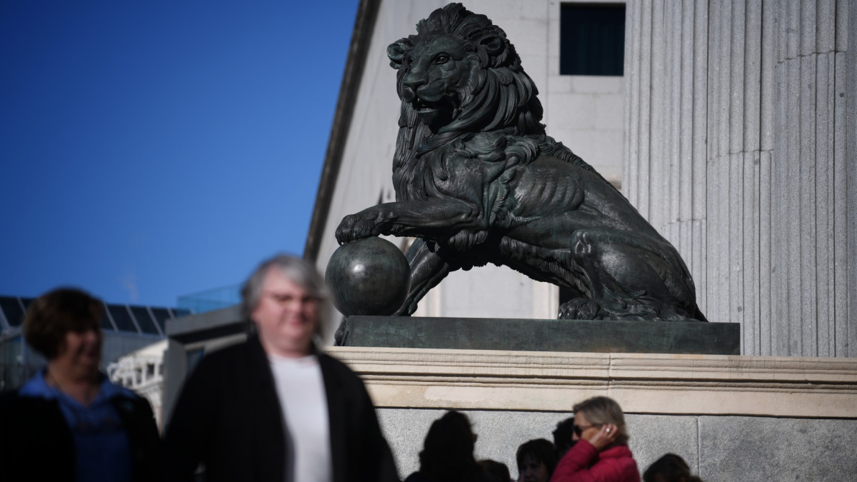 Vista de uno de los leones del Congreso de los Diputados con personas paseando.